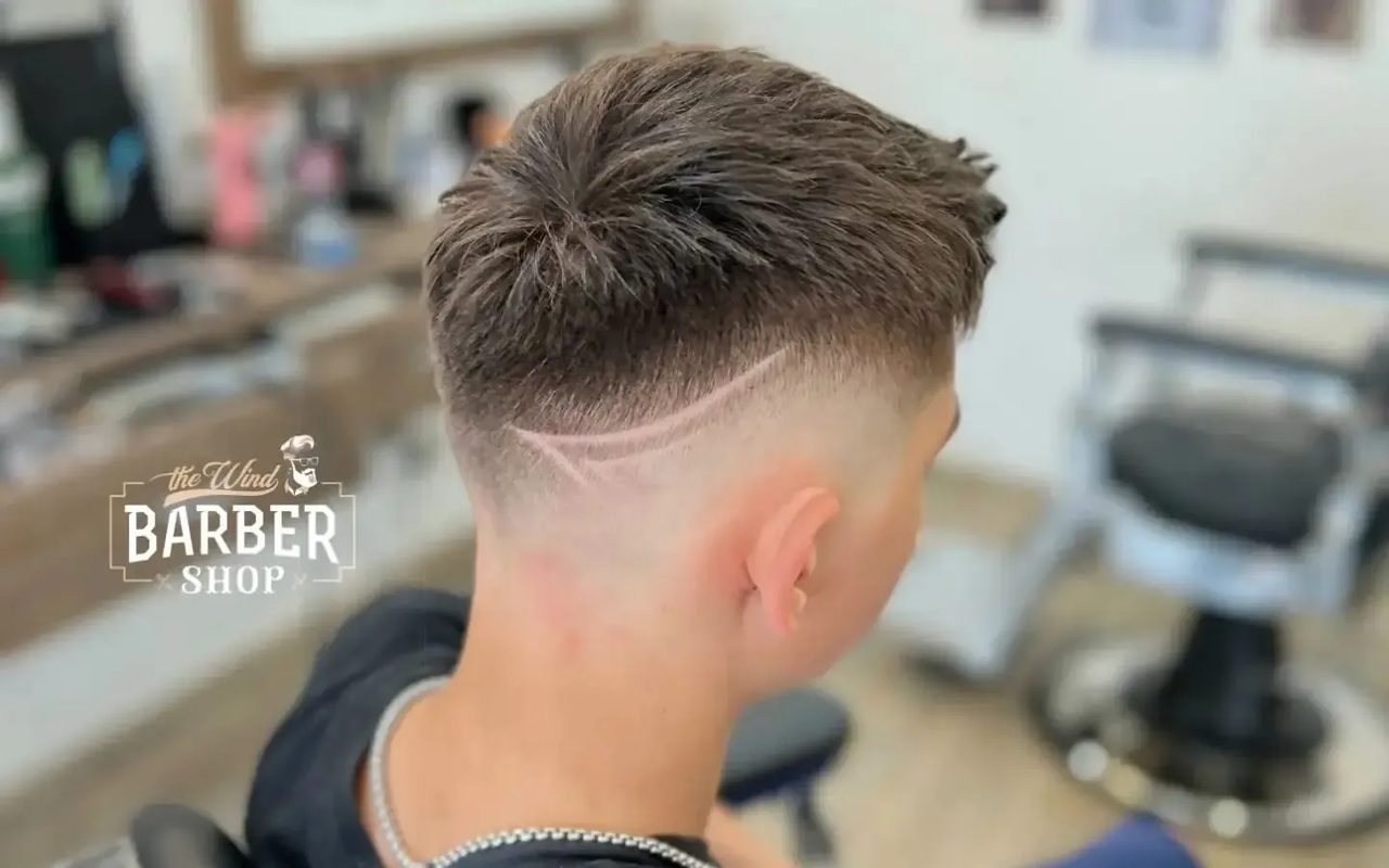 Klient s čerstvým high fade a vyholenou linkou, pohled zezadu; v pozadí křeslo barbershopu