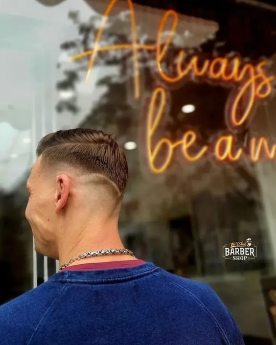 Skin fade s vyholenou linkou, v pozadí neon ve výloze