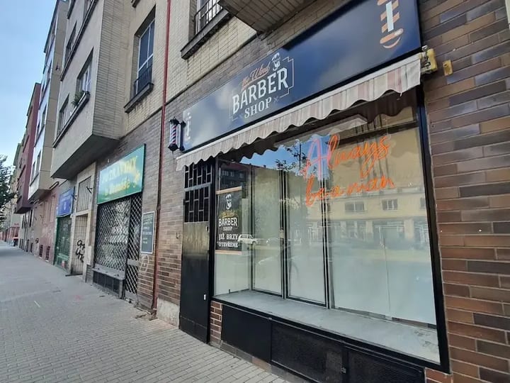 Provozovna The Wind Barber Shop z ulice, výloha s logem a markýzou